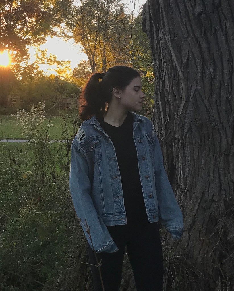girl wearing classic old ripped jean jacket by tree at sunset